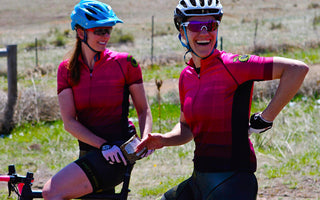 two women matching shirts smiling on bikes outside
